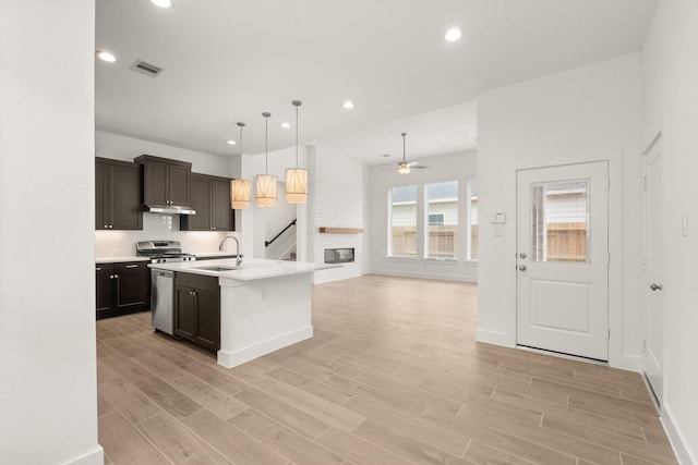 kitchen featuring light wood-style flooring, open floor plan, light countertops, a center island with sink, and pendant lighting