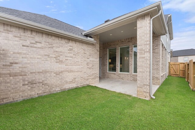 back of property with brick siding, a patio, a shingled roof, a lawn, and fence