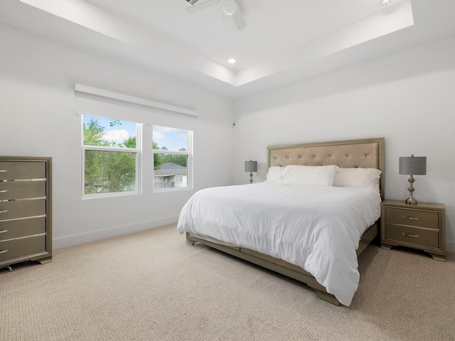 bedroom featuring ceiling fan, a tray ceiling, and light carpet