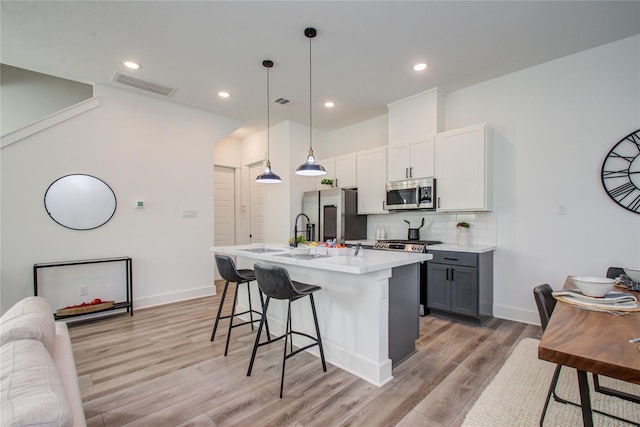 kitchen with light hardwood / wood-style flooring, appliances with stainless steel finishes, a kitchen breakfast bar, backsplash, and an island with sink