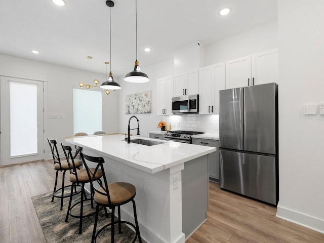 kitchen with appliances with stainless steel finishes, light stone countertops, a center island with sink, sink, and light hardwood / wood-style flooring