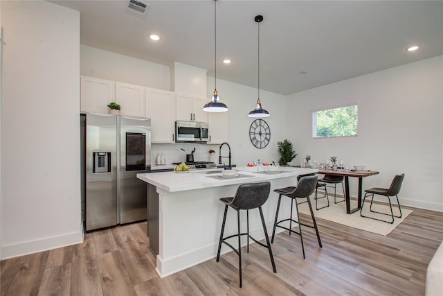 kitchen featuring appliances with stainless steel finishes, white cabinets, hanging light fixtures, backsplash, and light wood-type flooring