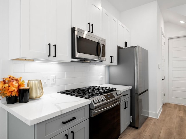 kitchen with appliances with stainless steel finishes, light stone countertops, tasteful backsplash, white cabinetry, and light hardwood / wood-style floors