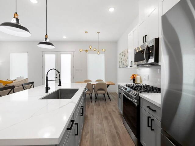 kitchen with appliances with stainless steel finishes, decorative light fixtures, decorative backsplash, and light hardwood / wood-style floors