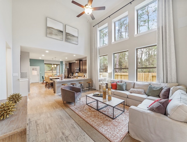 living room with ceiling fan, a towering ceiling, sink, and light hardwood / wood-style floors