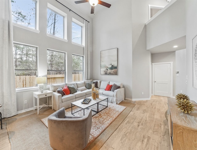 living room with light hardwood / wood-style flooring, ceiling fan, and a towering ceiling