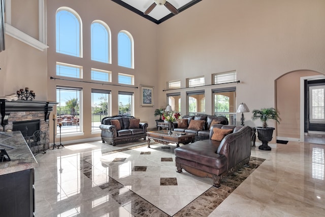 tiled living room with ceiling fan, a fireplace, and a high ceiling