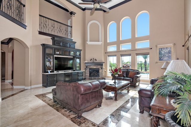 living room with light tile patterned flooring, a stone fireplace, ceiling fan, and a high ceiling