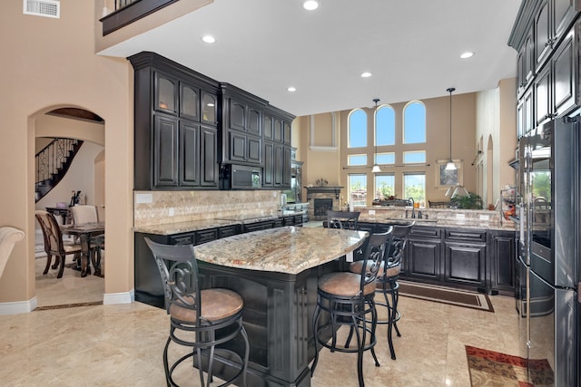 kitchen featuring tasteful backsplash, light stone counters, a kitchen island, kitchen peninsula, and a towering ceiling