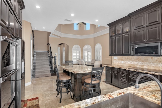 kitchen featuring decorative backsplash, a towering ceiling, light stone countertops, light tile patterned floors, and stainless steel appliances