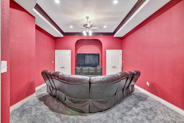 carpeted cinema room featuring ceiling fan, ornamental molding, and a tray ceiling