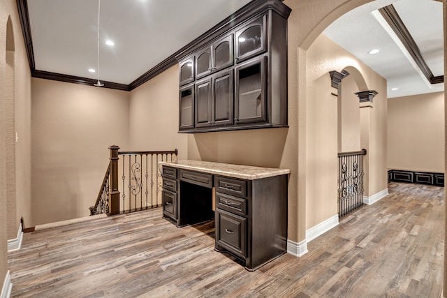 interior space with dark brown cabinets, ornamental molding, hardwood / wood-style flooring, and light stone countertops