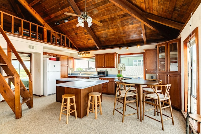 kitchen with a center island, brown cabinets, light countertops, glass insert cabinets, and white appliances