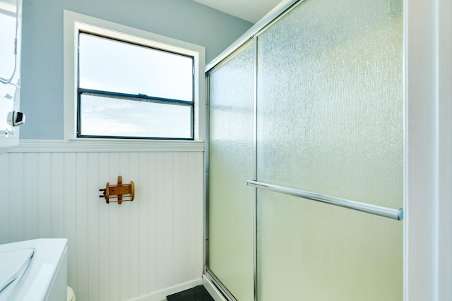 full bathroom featuring a stall shower, a wainscoted wall, and toilet