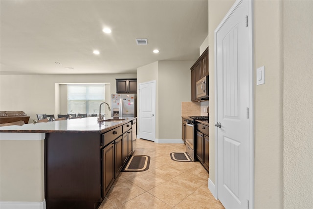 kitchen with a kitchen island with sink, appliances with stainless steel finishes, sink, light tile patterned flooring, and dark brown cabinetry