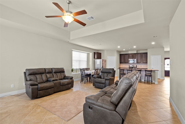 living room featuring ceiling fan, light tile patterned flooring, and a raised ceiling