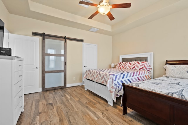 bedroom featuring ceiling fan, a barn door, a raised ceiling, and light hardwood / wood-style floors