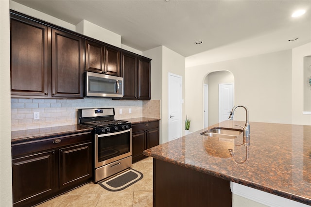 kitchen with stainless steel appliances, light tile patterned floors, decorative backsplash, sink, and dark stone counters