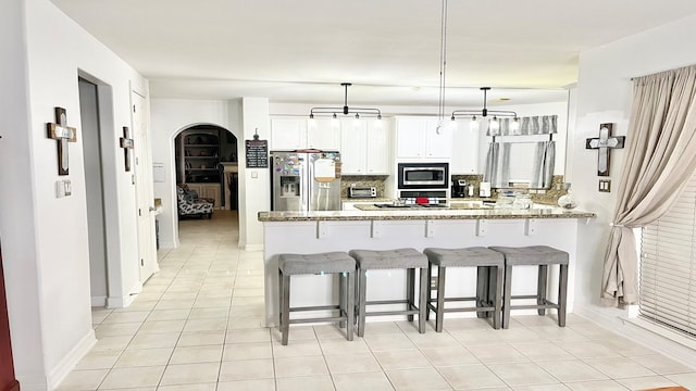 kitchen featuring white cabinetry, kitchen peninsula, hanging light fixtures, appliances with stainless steel finishes, and light stone countertops