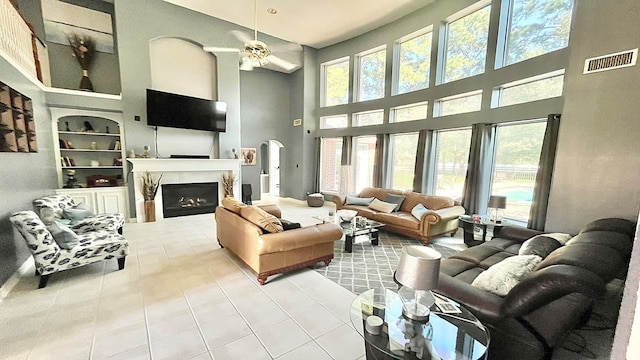 living room with ceiling fan, built in features, a high end fireplace, a high ceiling, and tile patterned flooring