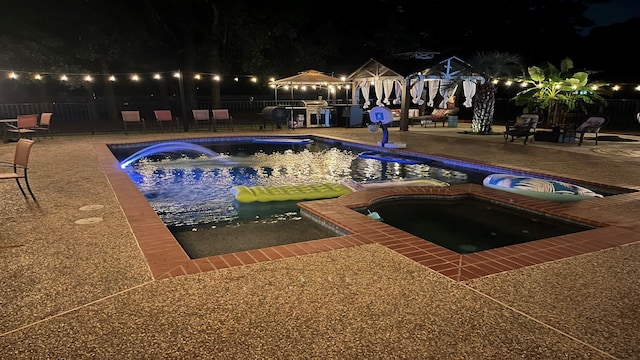 pool at night with an in ground hot tub and a patio area