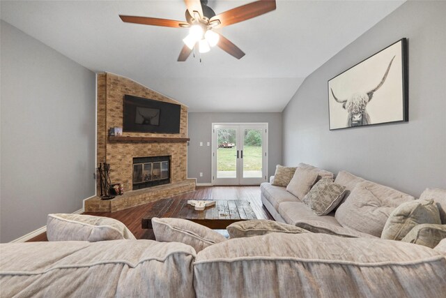 living room with a brick fireplace, wood-type flooring, vaulted ceiling, ceiling fan, and french doors