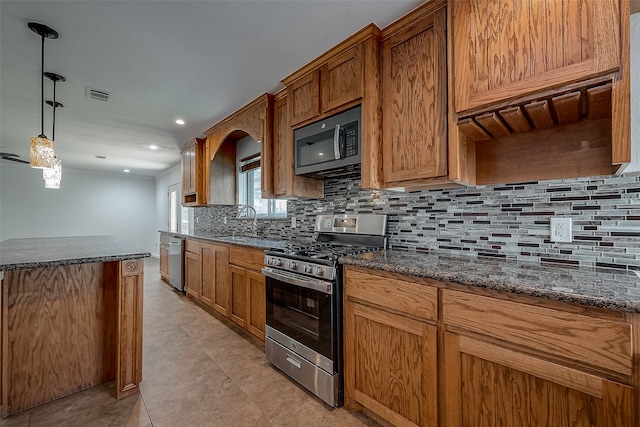 kitchen with dark stone countertops, stainless steel appliances, sink, light tile patterned flooring, and pendant lighting