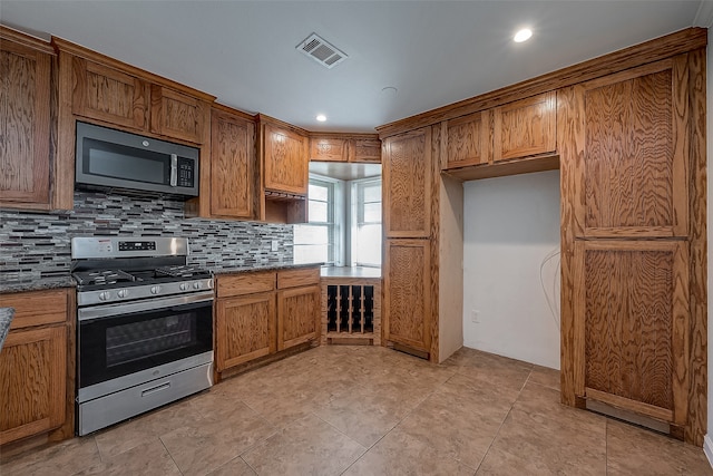 kitchen featuring appliances with stainless steel finishes, dark stone countertops, backsplash, and light tile patterned flooring