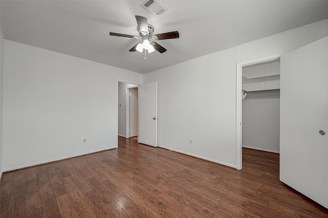 unfurnished bedroom featuring dark wood-type flooring, a walk in closet, ceiling fan, and a closet