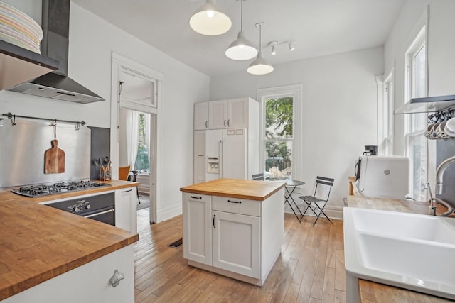 kitchen with stainless steel gas cooktop, white built in fridge, butcher block counters, a sink, and wall chimney range hood