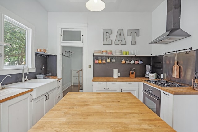 kitchen featuring oven, a sink, wood counters, white cabinetry, and wall chimney range hood