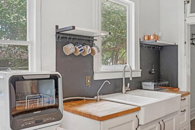 kitchen featuring sink, white cabinetry, wood counters, and a healthy amount of sunlight