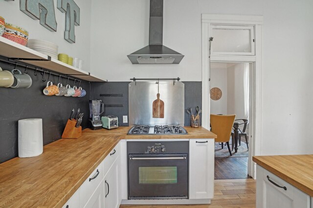 kitchen featuring butcher block counters, white cabinetry, wall chimney range hood, gas cooktop, and oven