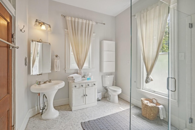 bathroom featuring toilet, a stall shower, plenty of natural light, and baseboards