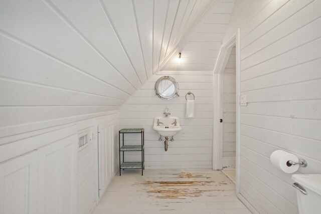 bathroom featuring wood walls, lofted ceiling, and toilet