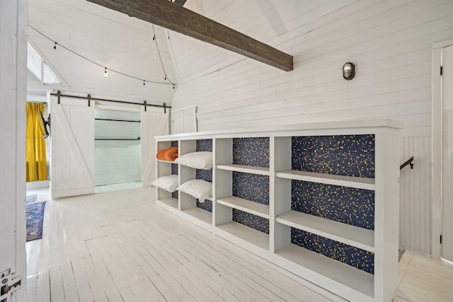 interior space with vaulted ceiling with beams, a barn door, wooden walls, and hardwood / wood-style floors