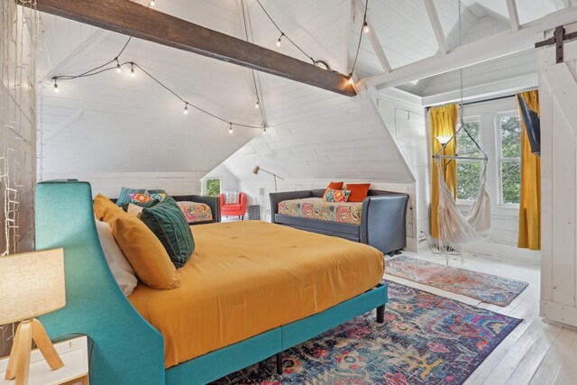 bedroom with a barn door, light hardwood / wood-style flooring, rail lighting, and vaulted ceiling with beams