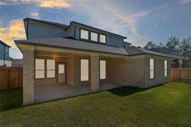 back house at dusk featuring a yard and a patio