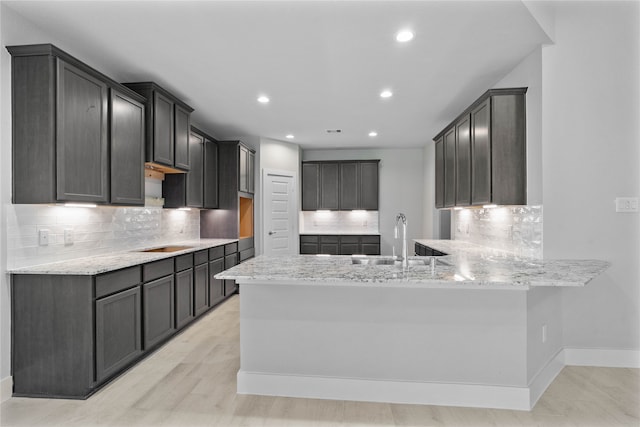 kitchen with kitchen peninsula, sink, tasteful backsplash, light stone countertops, and light hardwood / wood-style floors