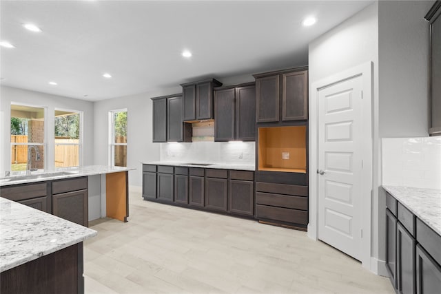 kitchen with sink, backsplash, dark brown cabinetry, and light stone counters