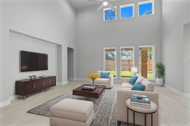 living room featuring ceiling fan, light hardwood / wood-style floors, and a towering ceiling