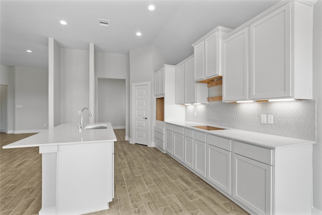 kitchen featuring light hardwood / wood-style floors, white cabinets, decorative backsplash, sink, and an island with sink