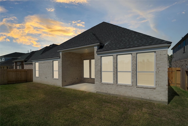 back house at dusk featuring a yard and a patio area