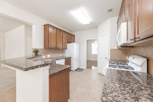 kitchen with dark stone countertops, white appliances, tasteful backsplash, light hardwood / wood-style flooring, and kitchen peninsula