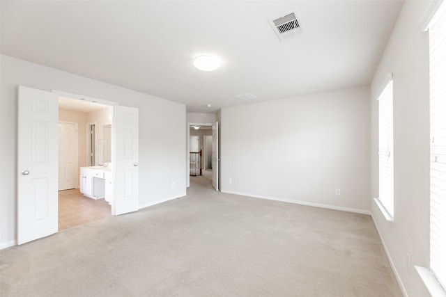 unfurnished bedroom featuring ensuite bath and light colored carpet