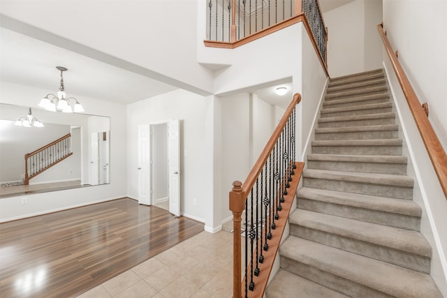 stairway featuring a towering ceiling, hardwood / wood-style floors, and an inviting chandelier