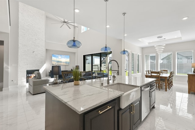 kitchen with hanging light fixtures, a stone fireplace, an island with sink, and a tray ceiling