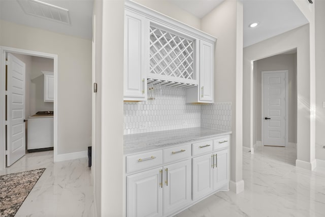 kitchen featuring light tile patterned floors, white cabinets, backsplash, washer / dryer, and light stone counters