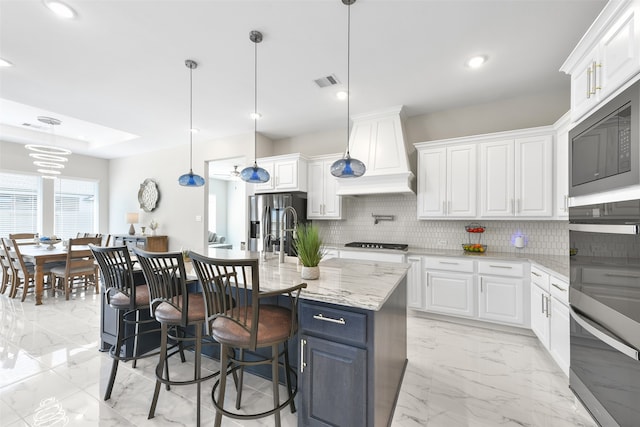 kitchen with decorative backsplash, light stone counters, white cabinets, pendant lighting, and premium range hood