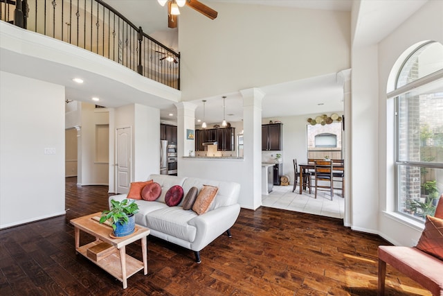 living room with decorative columns, ceiling fan, hardwood / wood-style flooring, and a towering ceiling